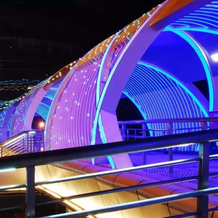Curved pedestrian bridge illuminated with blue and purple linear lighting